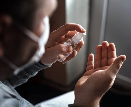 A person with a facial mask puts a disinfectant on his hand to protect against viral germs. Stop the coronavirus epidemic. Health and prevention of influenza and an infectious outbreak. Coronavirus Prevention Concept, Covid 19.の写真素材