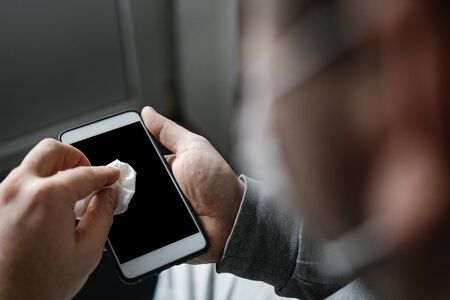 Masked man cleaning smartphone screen with alcohol or disinfectant. The concept of cleaning a dirty phone screen to prevent diseases from infectious bacteria. coronavirus covid 19.の写真素材