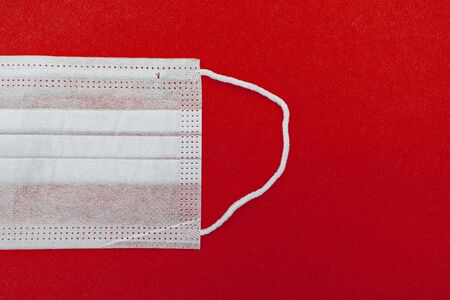 Medical disposable face mask on a red background with place for text. coronavirus covid 19. World pandemic coronavirus. Stop the pandemic. Health and prevention of influenza and an infectious outbreak. Quarantine. New 2019 nCoV virus.の写真素材
