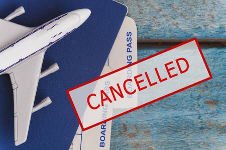 airplane, passport and tickets with a stamp in red text CANCELED on a blue wooden background. Flights canceled due to coronavirus outbreak. The influence of Covid-19 on the tourism industry.の写真素材