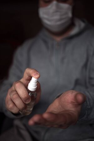 A person with a facial mask puts a disinfectant on his hand to protect against viral germs. Stop the coronavirus epidemic. Health and prevention of influenza and an infectious outbreak. Coronavirus Prevention Concept, Covid 19.の写真素材