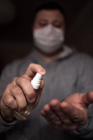 A person with a facial mask puts a disinfectant on his hand to protect against viral germs. Stop the coronavirus epidemic. Health and prevention of influenza and an infectious outbreak. Coronavirus Prevention Concept, Covid 19.の写真素材