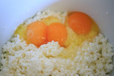 In a bowl of cottage cheese, eggs on a wooden table for making homemade cheesecakesの写真素材