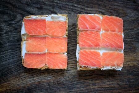 Two whole grain bread toasts with cream cheese and lightly salted salmon on a dark wooden board. Flat lay. Copy space. Concept, healthy breakfast, food, snack.の写真素材