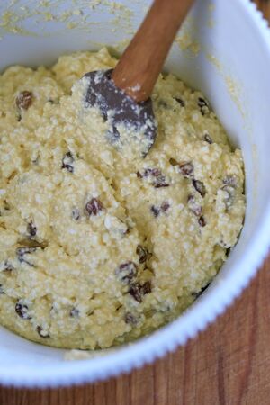 The dough for making Russian traditional home-made cottage cheese pancakes with raisins on a wooden table is kneaded in a bowlの写真素材