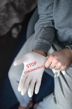 Man in gray clothes putting on medical latex gloves with red text STOP CORONAVIRUS. Concept, prevention and protection against Covid-19 infectionの写真素材