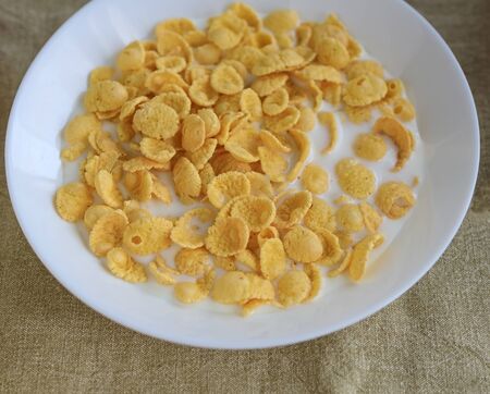 Cornflakes in milk in a white plate on a plain linen tablecloth. Close-up. View from above.の写真素材