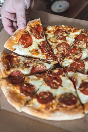 Cropped man takes a piece of pizza with his hand. Selective focus, blur, closeupの写真素材
