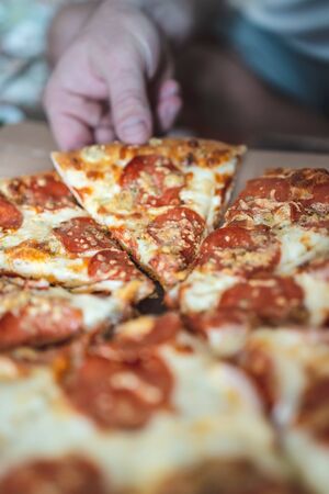 Cropped man takes a piece of pizza with his hand. Selective focus, blur, closeupの写真素材