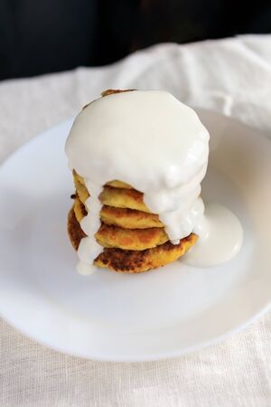 On the table with a linen light tablecloth, curd pancakes, pancakes in a plate are watered with sour cream sauce. Concept, simple healthy breakfast. Copy space. View from aboveの写真素材