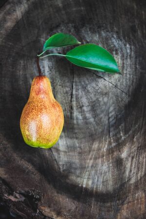 One juicy ripe pear with leaves lies on a wooden vintage dark background. Top view, copy space.の写真素材