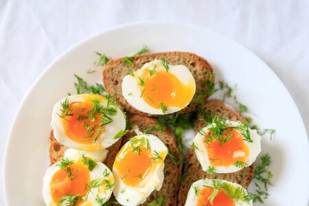 Soft-boiled egg halves with dill on whole grain toast bread on a white plate. Close-up, top view. Healthy, healthy and healthy breakfast concept.の写真素材