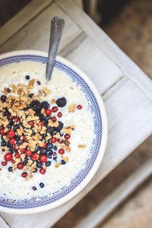 bowl with blue national pattern with cottage cheese and yogurt smoothie with chia, raspberries, red currants, blueberries, blackberries, walnuts on a white wooden table. Top view, close up.の写真素材