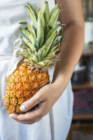 cropped young woman in a white cook apron holding a ripe and juicy pineapple in her hands.の写真素材