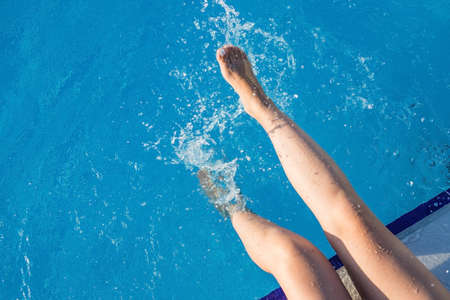cropped young european woman kicks in the pool splashes water. Concept, carefree, summer, vacation. Copy space. View from aboveの写真素材