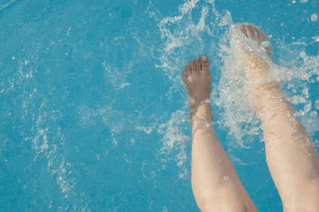 cropped young european woman kicks in the pool splashes water. Concept, carefree, summer, vacation. Copy space. View from aboveの写真素材