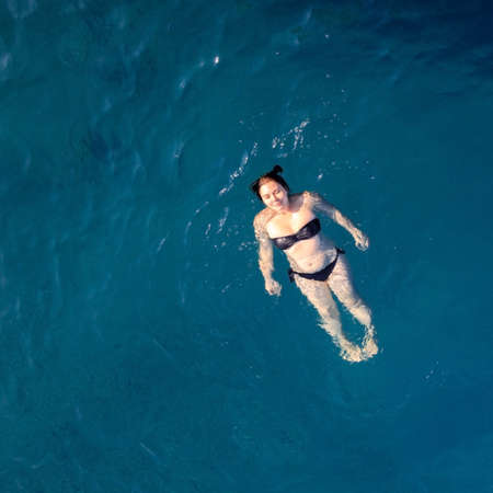 aerial top view happy young woman in black swimsuit swims in the Red Sea, Egypt, Sharm el Sheikh. Vacation and adventure. Blue water. Top view of a lazy girl resting in the sea-ocean. Copy spaceの写真素材