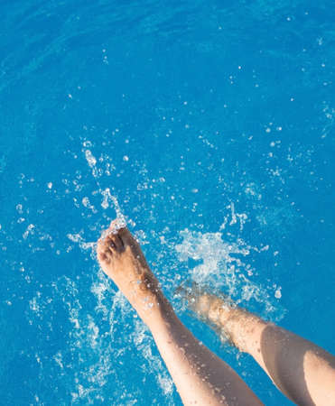 cropped young european woman kicks in the pool splashes water. Concept, carefree, summer, vacation. Copy space. View from aboveの写真素材