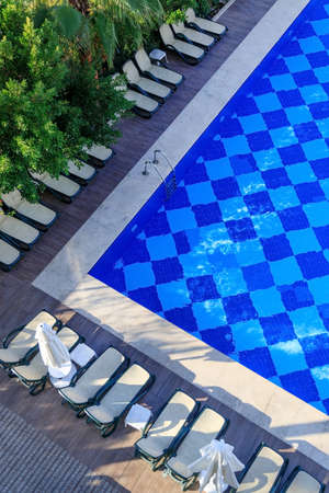 Top view of the pool, sun loungers and umbrellas among lush green palms and bushes in a resort hotel...