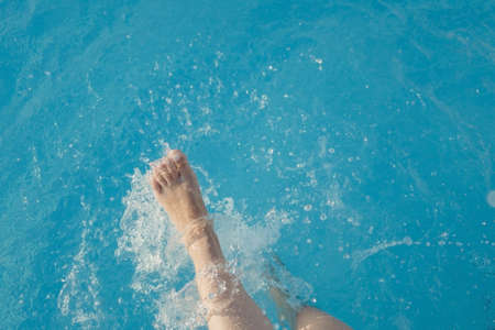 cropped young european woman kicks in the pool splashes water. Concept, carefree, summer, vacation. Copy space. View from aboveの写真素材