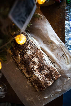 Traditional Christmas chocolate roll with cream on a background of Christmas tree lights on a dark background. View from aboveの写真素材