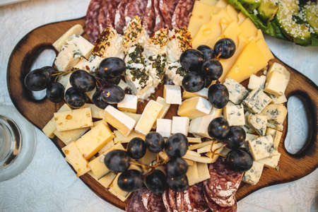 Cheese and meat platter on a wooden board on a festive table. View from above.の写真素材