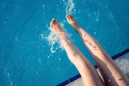 cropped young european woman kicks in the pool splashes water. Concept, carefree, summer, vacation. Copy space. View from aboveの写真素材