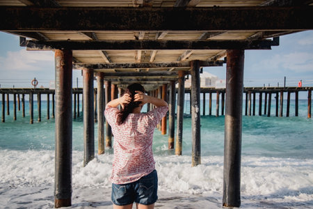 Turkey, Mediterranean Sea. Young woman turned away from the camera, running away from the waves under a wooden pier.の写真素材