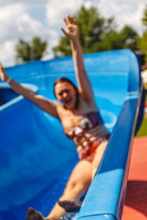 Happy young plump caucasian woman rides with raised hands on a water slide in a water park. Photo in...