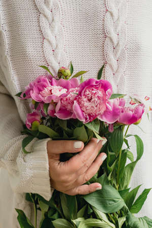 cropped young woman in white knitted sweater holding a bouquet of fresh flowers pink peonies