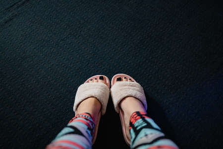 female feet with black pedicure in pink fluffy slippers on a dark semi-background, top view, copy...