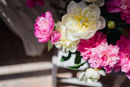 a bouquet of fresh white and pink peonies in a transparent glass vase with beautiful shadows near a white curtain tulle, in blurの写真素材
