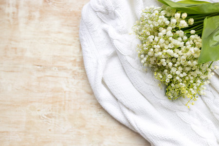 a bouquet of fresh lilies of the valley lies on a white knitted sweater on a light wooden background, top view. Copy spaceの写真素材