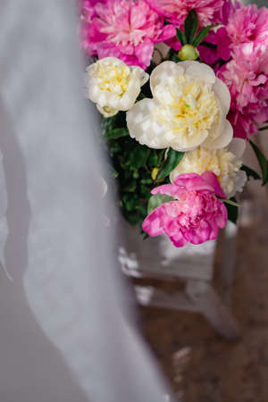 a bouquet of fresh white and pink peonies in a transparent glass vase with beautiful shadows near a white curtain tulle, in blurの写真素材