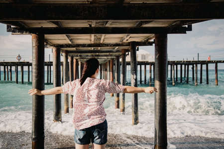 Turkey, Mediterranean Sea. Young woman turned away from the camera, running away from the waves under a wooden pierの写真素材