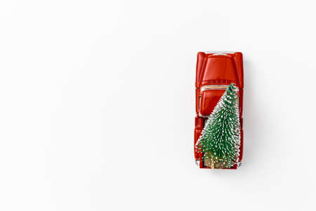 miniature red car in the back carries a Christmas tree on a white isolated background, top view. Save the space. Concept, festive Christmas mood, gift delivery. The trendの写真素材