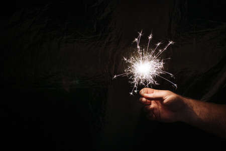 Hand with sparkler on dark background. Celebrating new year with sparkler. Hand holding sparkler on dark background. Christmas fun. New year concept.の写真素材