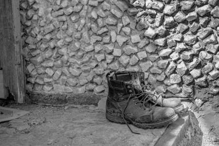 old dirty worn men's military motorcycle boots stand on the doorstep of the house. monochrome, black and white photo.の写真素材