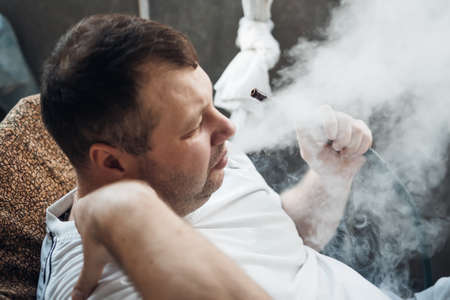 happy caucasian white young man smoking hookah and blowing smoke.の写真素材