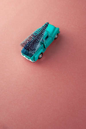 miniature green-aquamarine car in the back carries a Christmas tree on a peach-pink isolated background, top view. Save the space. Concept, festive Christmas mood, gift delivery. The trendの写真素材
