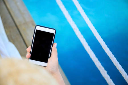 female hand holding a phone - smartphone on a blue sea background.の写真素材