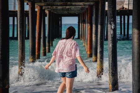 Turkey, Mediterranean Sea. Young woman turned away from the camera, running away from the waves under a wooden pier.の写真素材