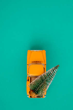 a miniature yellow car in the back carries a Christmas tree on a simple blue-aquamarine background, top view. Save the space. Concept, festive Christmas mood, gift delivery. The trendの写真素材