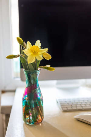 on a desktop with a monitor and keyboard, in a home office, there is a stained glass vase with fresh...