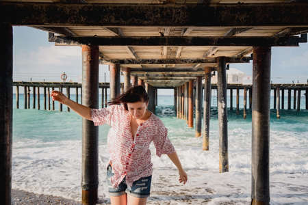 Turkey, Mediterranean Sea. Young woman turned away from the camera, running away from the waves under a wooden pier.の写真素材