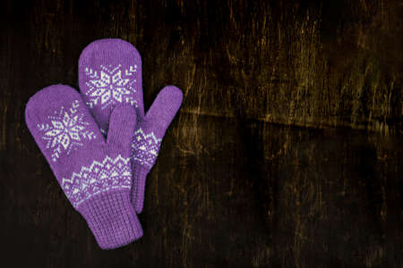 a pair of red-pink-lilac-magenta purple knitted mittens on a dark blue-green-brown wooden vintage background, copy space.の写真素材