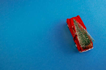 a miniature red car in the back carries a Christmas tree on a simple blue-aquamarine background, top view. Save the space. Concept, festive Christmas mood, gift delivery. The trend.の写真素材