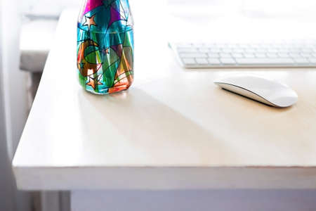 on a desktop with a monitor and keyboard, in a home office, there is a stained glass vase with fresh flowers of yellow daffodils. Concept, enjoyable work online remotely.の写真素材