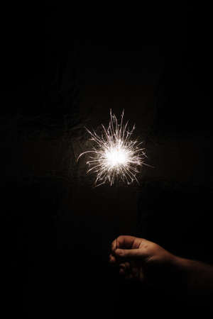 Hand with sparkler on dark background. Celebrating new year with sparkler. Hand holding sparkler on dark background. Christmas fun. New year concept.の写真素材