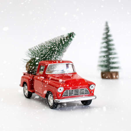 miniature red car in the back carries a Christmas tree on a white isolated background under snow, top view. Save the space. Concept, festive Christmas mood, gift delivery. The trendの写真素材